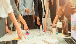 Adults brainstorming - standing around table pointing to different words on sheet of paper